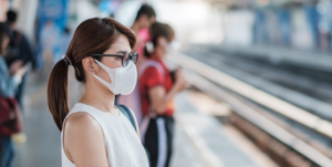 mulher de roupas brancas e óculos usando máscara em estação de trem