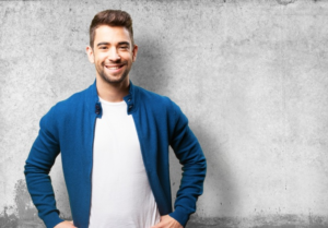 homem de casaco azul sorrindo de costas para parede cinza