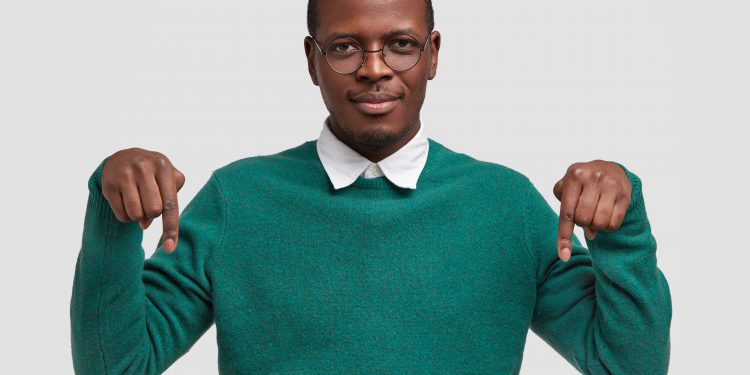 a visao horizontal de um cara de pele escura satisfeito demonstra algo no chao aponta com os dois dedos indicadores scaled