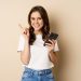 elegante jovem moderna segurando o celular apontando o dedo para a esquerda e sorrindo o conceito de compras scaled