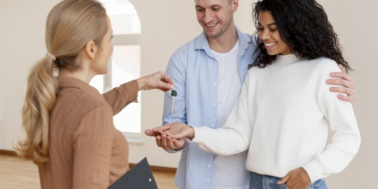 corretor de imoveis entregando a um casal sorridente as chaves de sua nova casa scaled