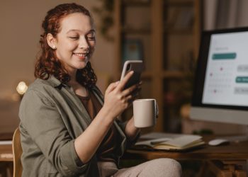 woman home using smartphone front computer while having coffee scaled