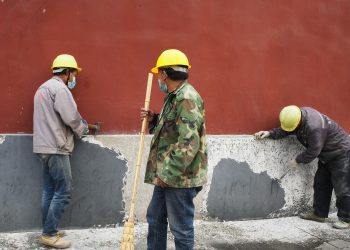 Três homens concertando pintura de parede.