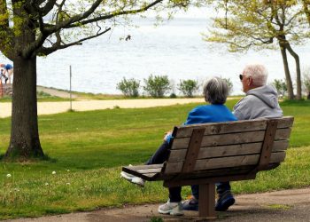 Casal de idosos sentados em banco de praça tranquilos.