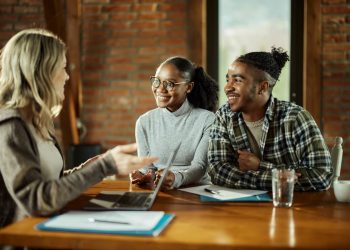 Um casal sentado em uma mesa, conversando com uma mulher que está falando sobre o seguro de vida