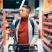 Um homem no supermercado com um carrinho e o celular na mão