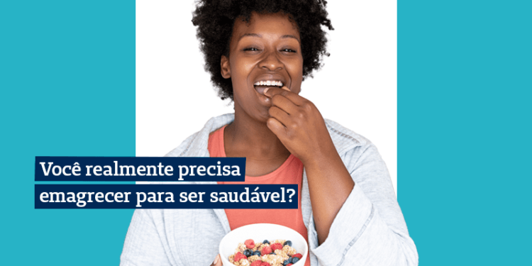 mulher segurando com uma mão um pote branco com frutas enquanto sorri e coloca uma fruta na boca com a outra mão