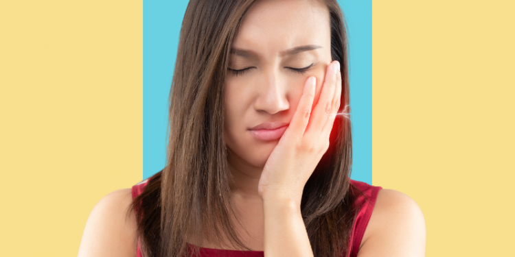 mulher com a mão sobre a bochecha e expressão de dor por causa da boca inchada