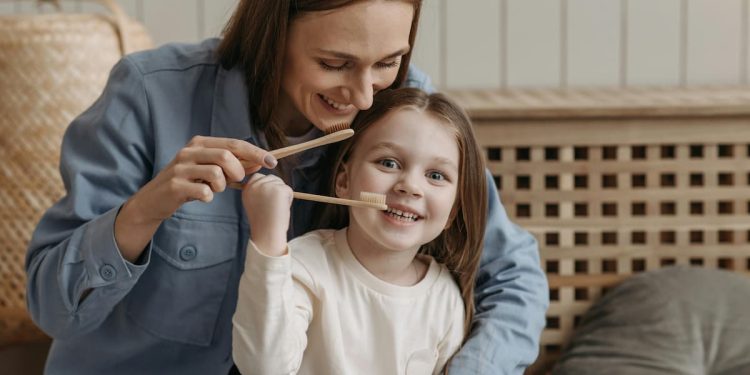 Mãe e filha segurando escova de dente fazendo a higiene bucal.