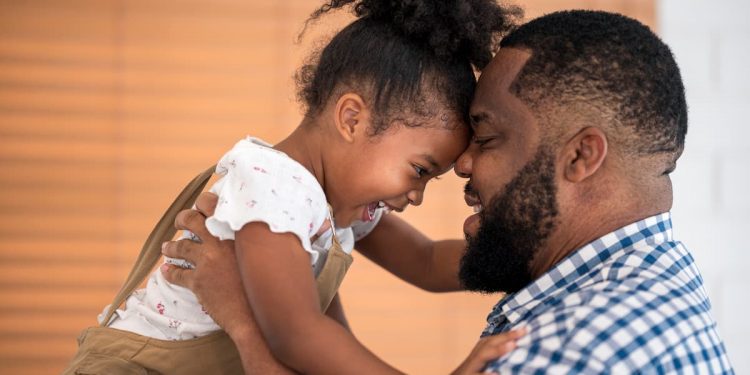 O pai com a filha no colo com as testas juntas e sorrindo
