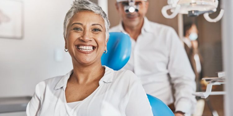 Uma senhora em um consultório odontológico, com o dentista atrás dela