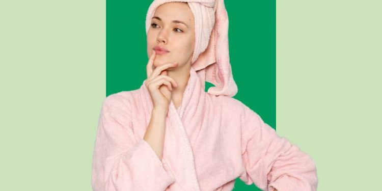 Uma mulher de roupão rosa na frente de um fundo verde.