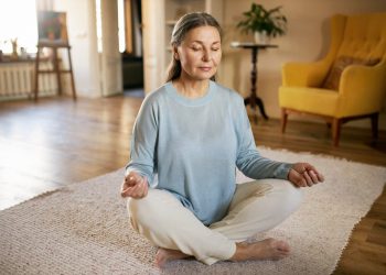 Uma senhora meditando no chão da sua sala