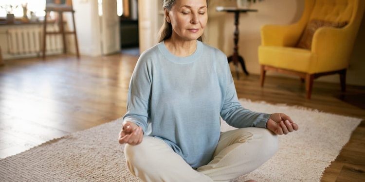 Uma senhora meditando no chão da sua sala
