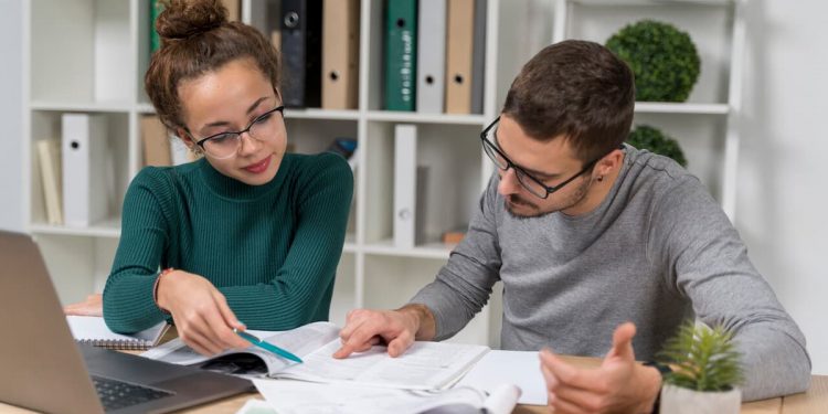 Um casal analisando uns papéis com um computador em cima da mesa