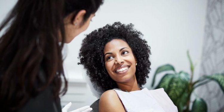 Uma mulher no consultório odontológico deitada na cadeira, sorrindo para a dentista