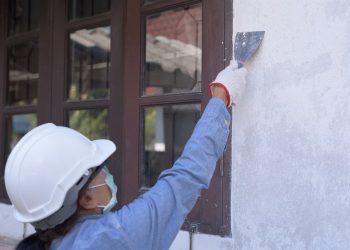 Uma mulher com capacete de obra, cobrindo uma rachadura na parede
