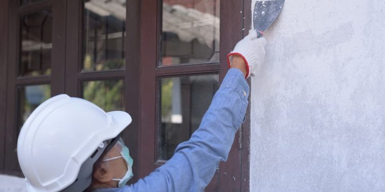 Uma mulher com capacete de obra, cobrindo uma rachadura na parede