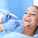 Uma mulher deitada na cadeira de um consultório odontológico, sendo analisada pela dentista