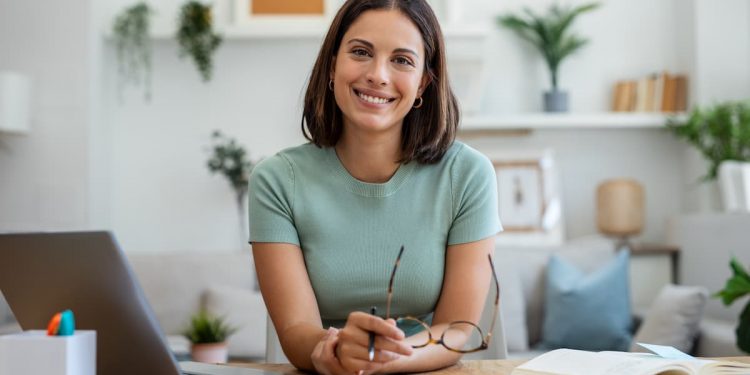 Uma mulher sentada, na sua frente uma mesa de escritório, com notebook, papéis