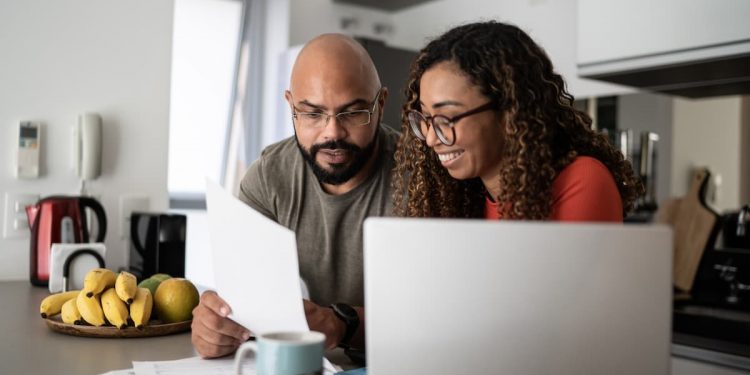 Um casal sentado lendo um papel e mexendo no computador
