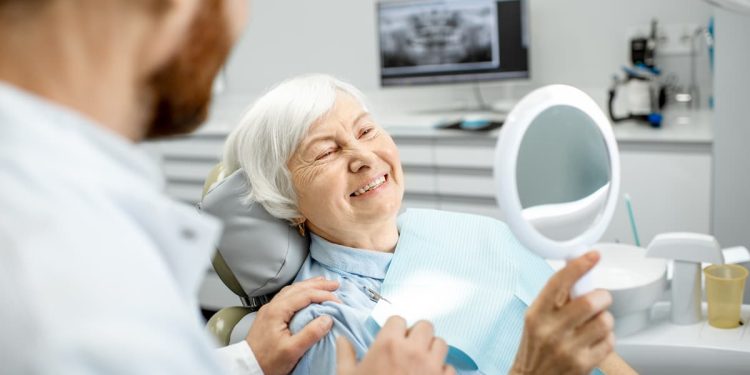 Uma senhora na cedeira de um consultório odontológico, sorrindo para o espelho