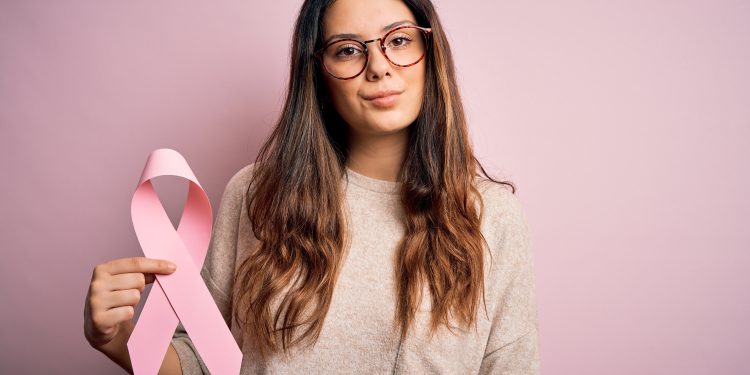 mulher de cabelos longos e óculos de grau, segurando fita rosa que representa o outubro rosa