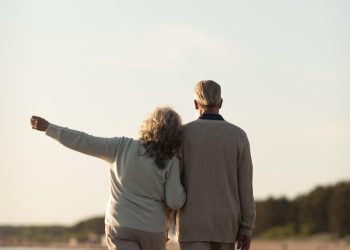 foto mostra casal na terceira idade, com homem e mulher, caminhando de braços dados
