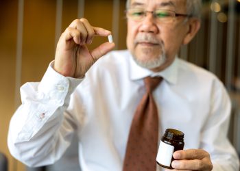 Senhor de blusa branca, com um remédio na mão.