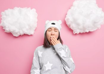 Fundo rosa com uma menina de pijama abrindo a boca e tampando-a com a mão