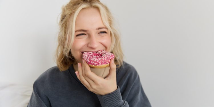 Mulher loira mordendo cupcake rosa