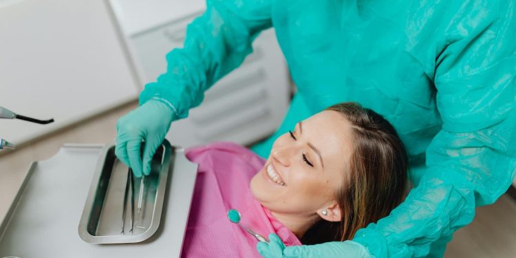 Mulher sorrindo em mesa de consultório odontológico com dentista.