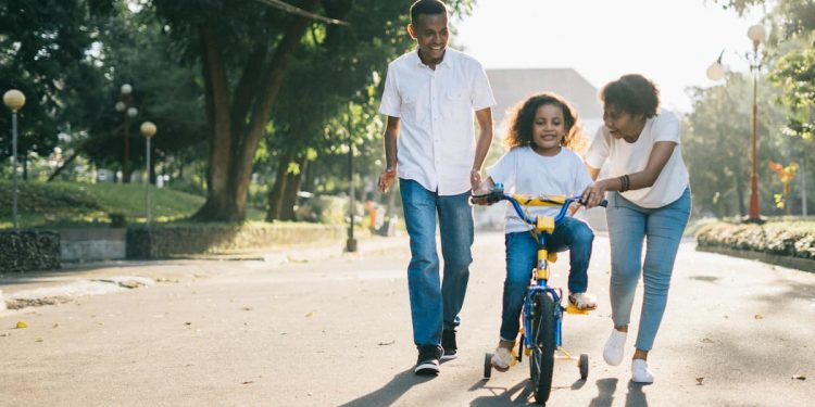 Família, pai, mãe e filha, feliz com a menina andando de bicicleta.