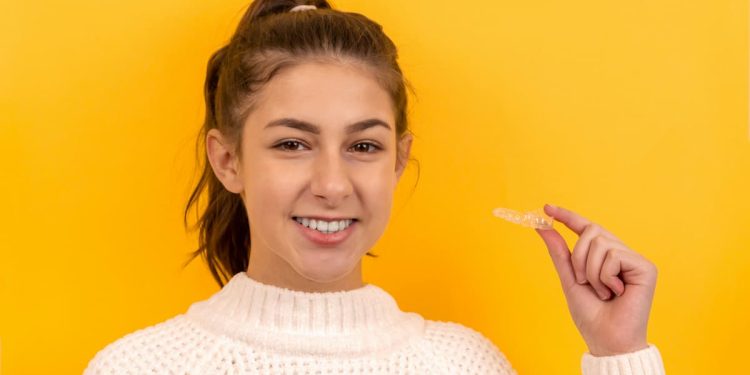 Menina em um fundo amarelo segurando um aparelho invisível.