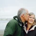 Casal de idosos em uma praia com ele beijando o rosto dela.