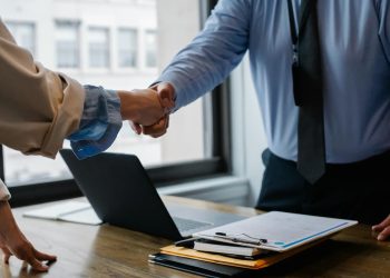 Duas pessoas dando a mão em um escritório empresarial.
