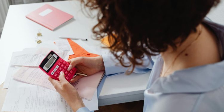 Mulher sentada em mesa usando calculadora e com documentos.