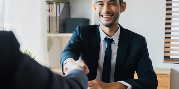 Homem em escritório de terno dando as mãos com contrato.