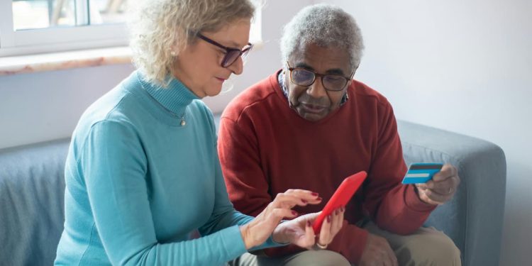 Casal de idosos com tablet e cartão de crédito fazendo pagamentos.