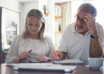Casal de idosos sentados na mesa fazendo conta em calculadora.