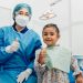 Dentista e criança feliz em consultório odontológico.