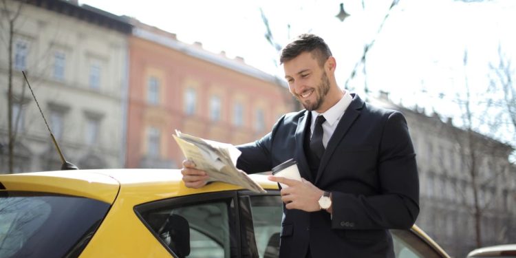 Homem feliz lendo jornal com café com seu carro.