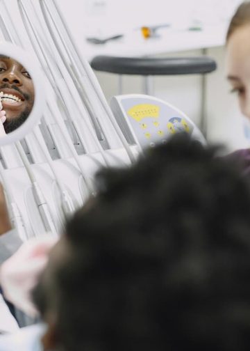 Homem sorrindo em espelho de consultório odontológico com dentista.