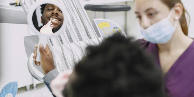 Homem sorrindo em espelho de consultório odontológico com dentista.
