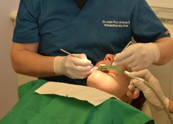 Paciente em cadeira com dentista realizando procedimento na boca.