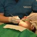 Paciente em cadeira com dentista realizando procedimento na boca.