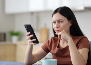 Mulher sentada com expressão preocupada olhando para o celular.