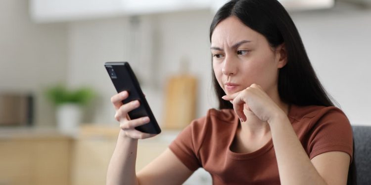 Mulher sentada com expressão preocupada olhando para o celular.