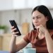 Mulher sentada com expressão preocupada olhando para o celular.