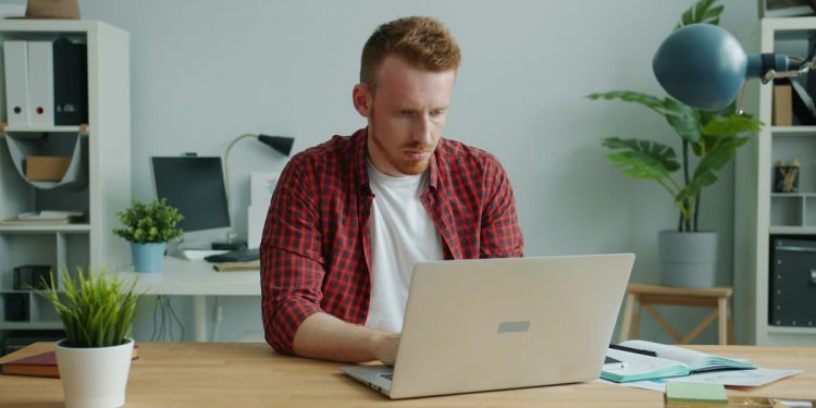 Homem sentado em mesa de escritório mexendo em notebook.